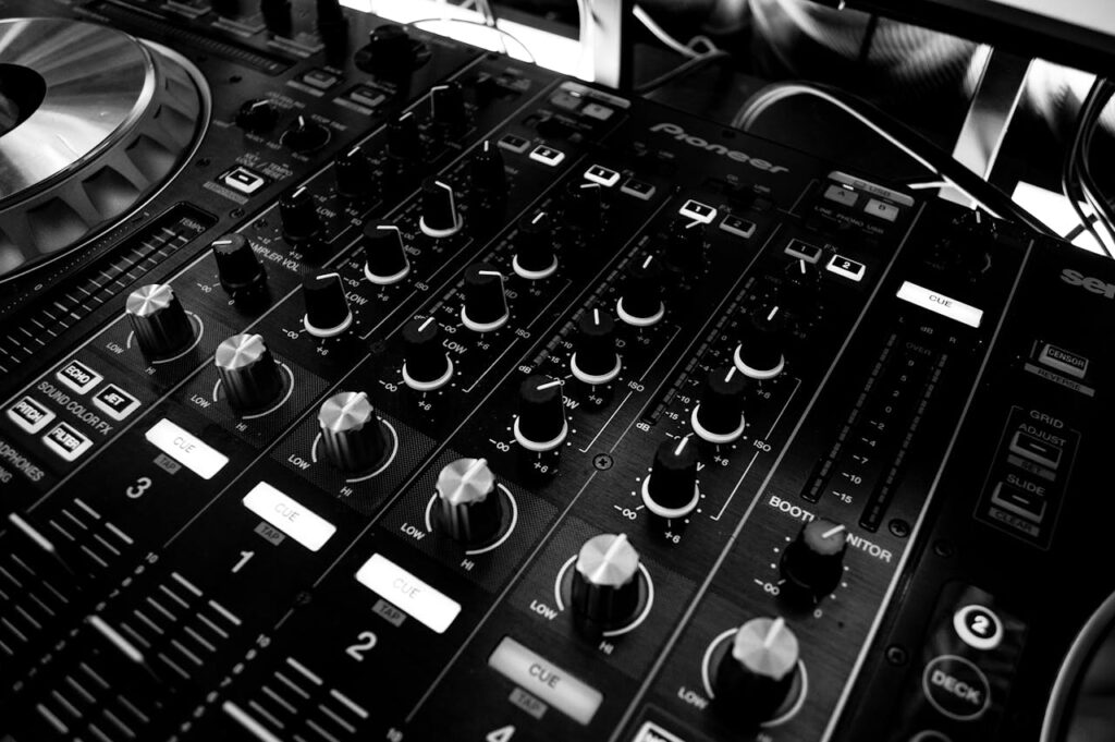 pexels-photo-63703 Black and white close-up of a DJ's audio mixing console with knobs and controls.